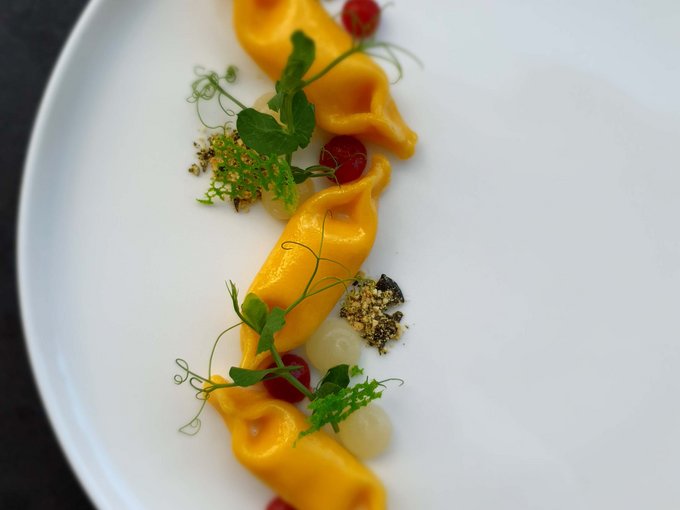 Settimane del Gusto Tre ravioli farcite con decorazioni su piatto bianco presentate artisticamente