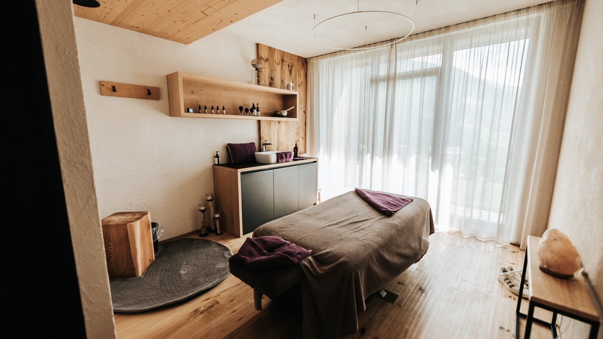 Das Wellnessbereich für Erwachsene Heller Massageraum mit Behandlungsliege und großen Fenstern mit Vorhängen