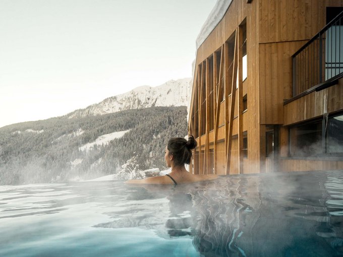 Der Erlebnisort Gassenhof Person entspannt im beheizten Außenpool mit Blick auf schneebedeckte Berge