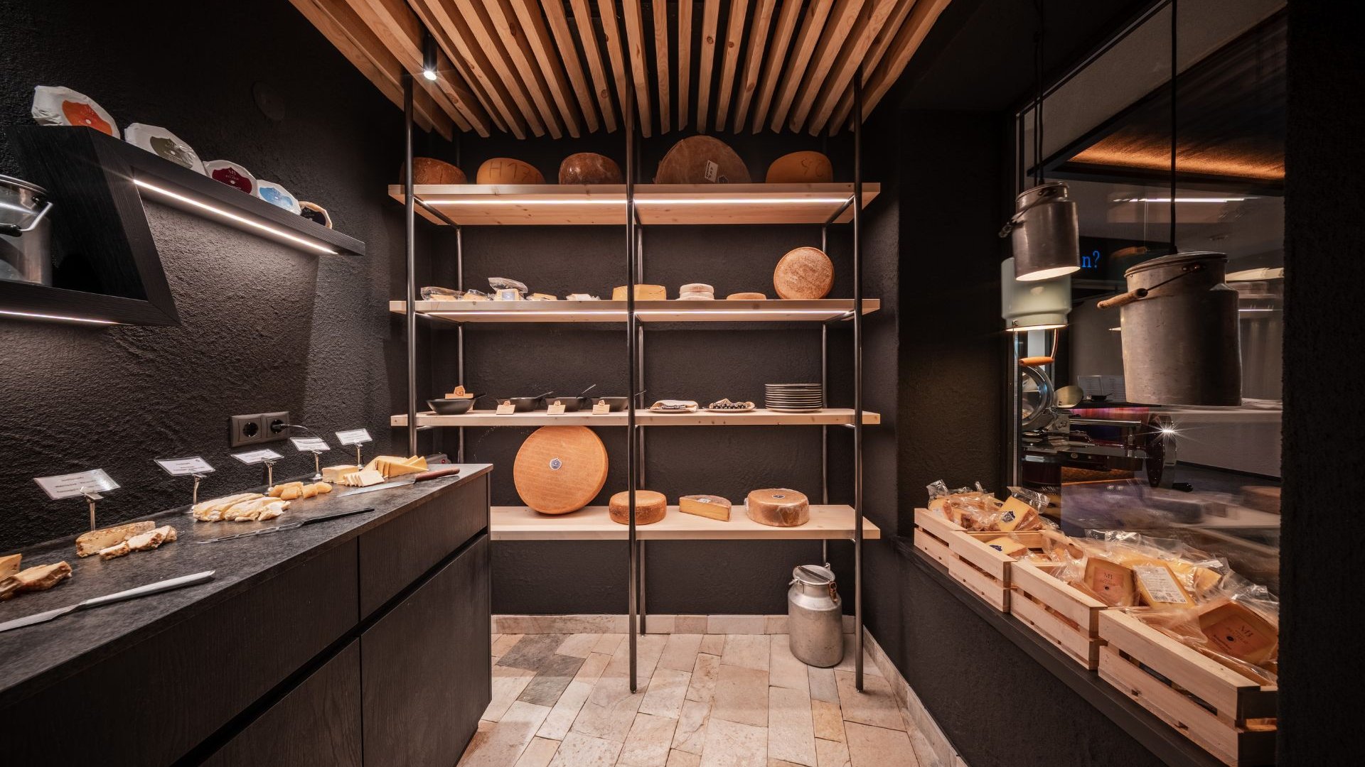 Neu bei uns im Gassenhof Dunkler Buffetbereich mit Regalen voller Brot, Käse und weiteren Lebensmitteln
