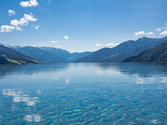 Hotel a Racines con centro benessere Acqua limpida di un lago circondato da montagne sotto un cielo azzurro