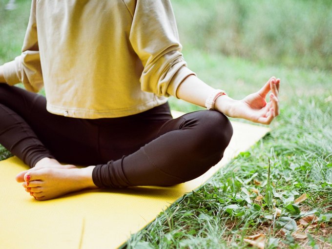 Fitness und Yoga Person meditiert im Lotussitz auf gelber Matte im Freien