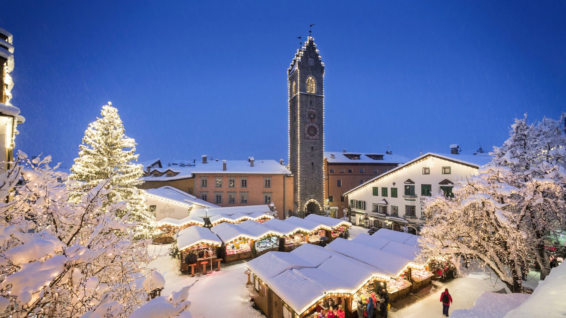 Urlaub bei Sterzing Winterlicher Weihnachtsmarkt mit beleuchtetem Turm und verschneiten Bäumen bei Nacht