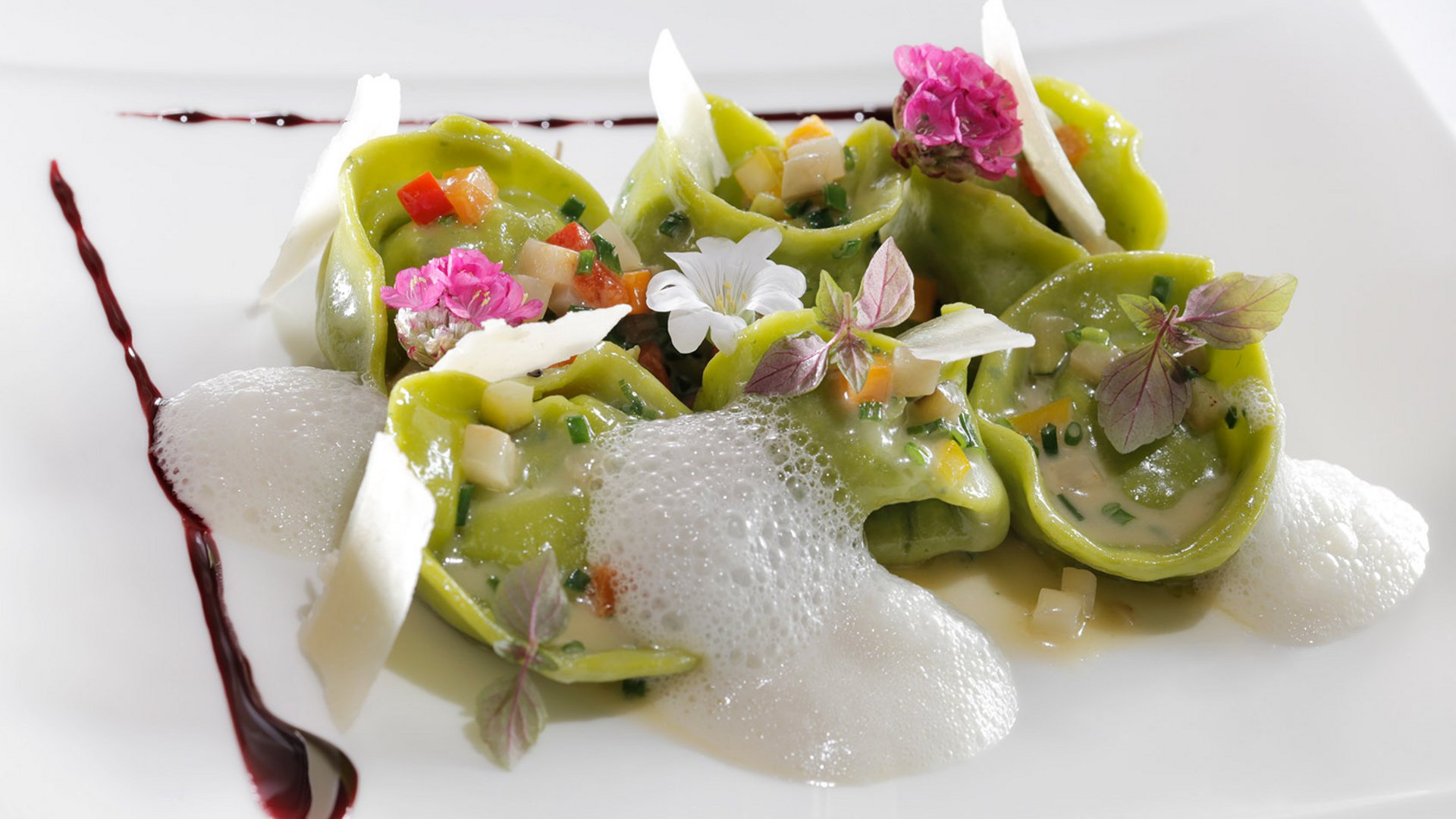 Ricette segrete Tortellini verdi con schiuma, verdure e fiori decorativi su piatto bianco