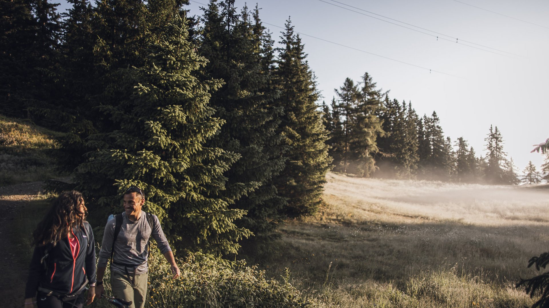 Your Vitalpina Hotel Two people hiking on a forest trail with sun and mist in the background