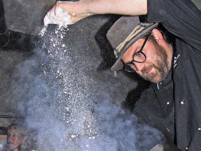 Traditional cuisine at Chalet Gratznhäusl Man wearing hat sprinkles flour into the air while cooking