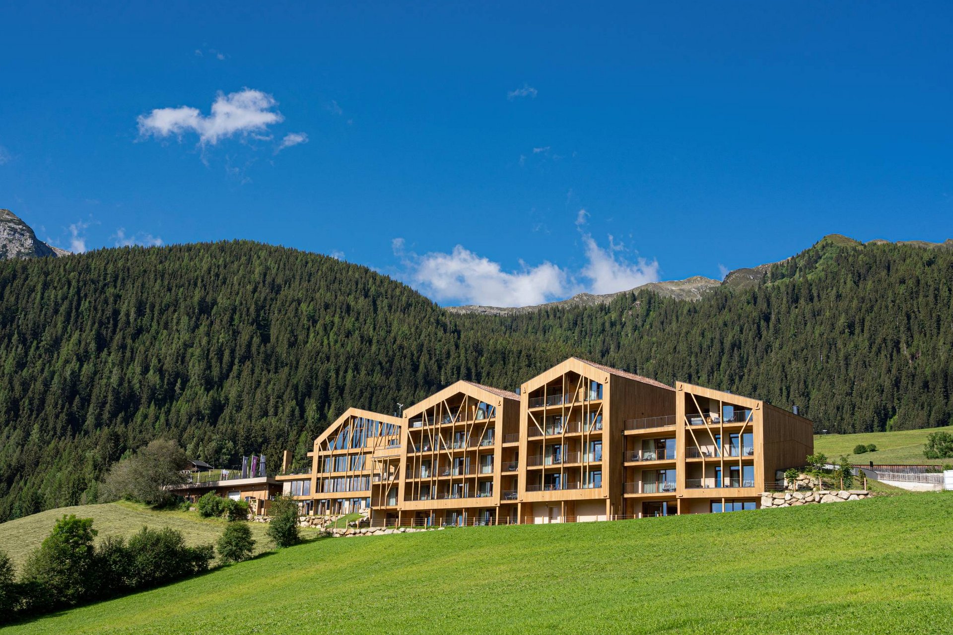 Urlaub anfragen Modernes Holzgebäude vor bewaldetem Berg und blauem Himmel