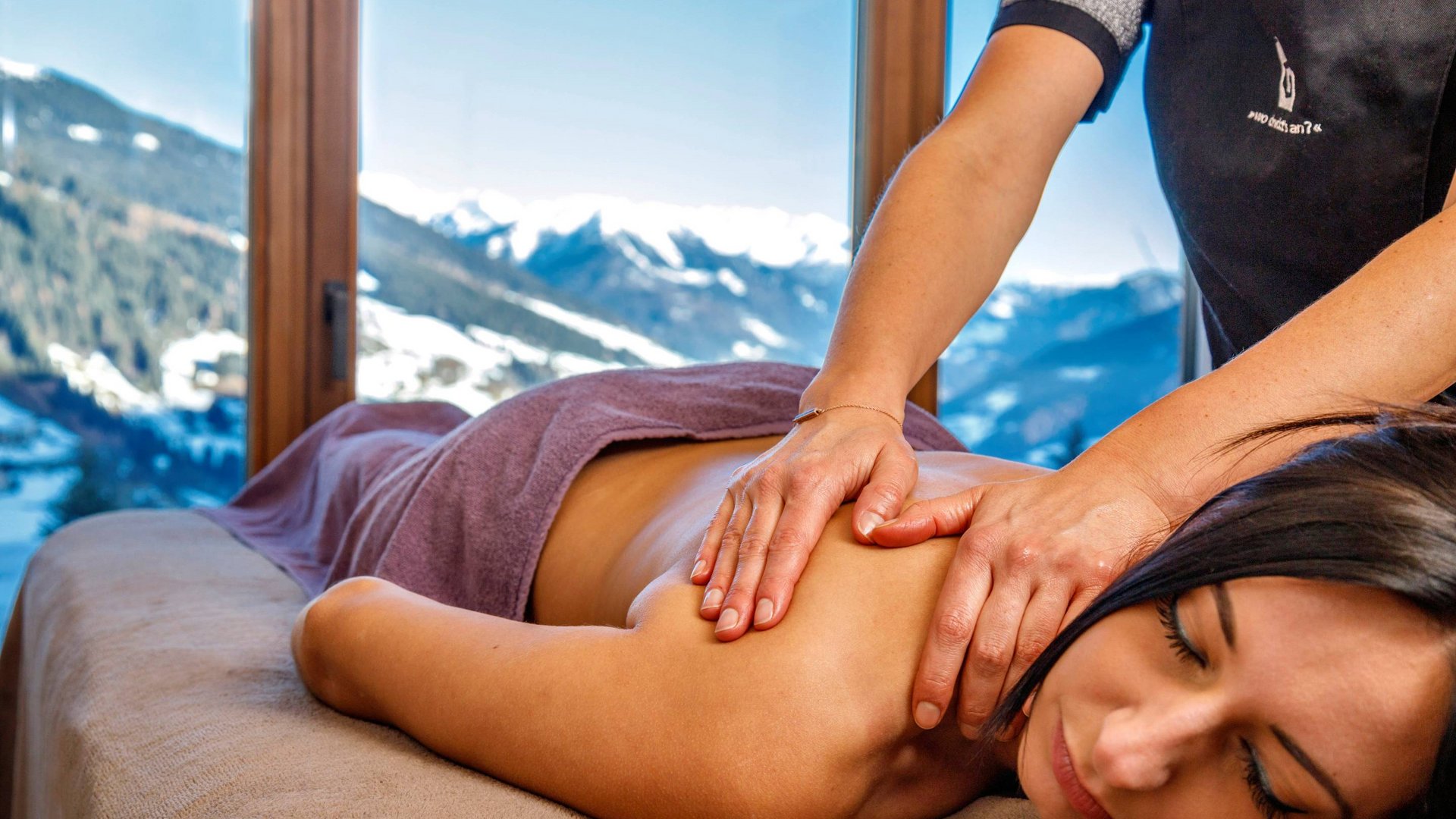 Frau bekommt Rückenmassage mit Bergblick durch großes Fenster