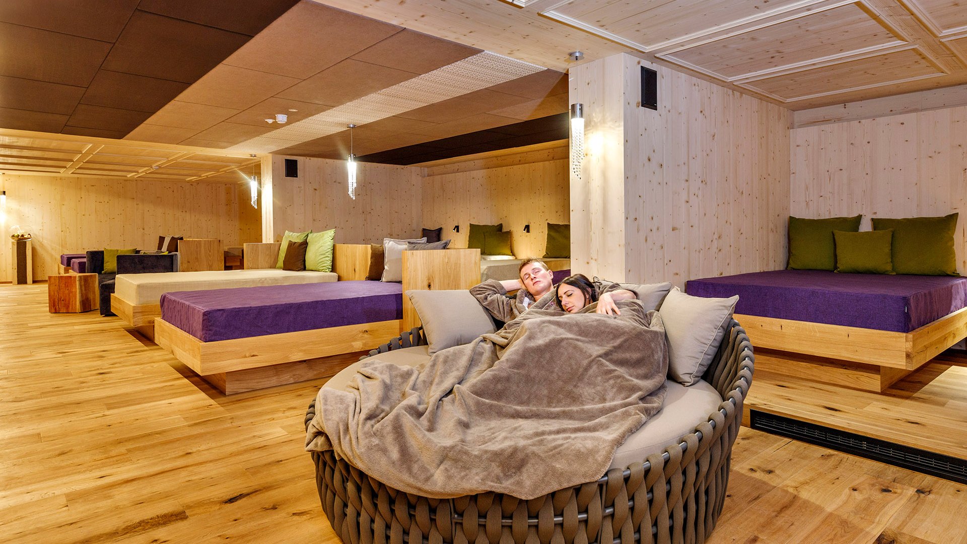 Das Logen-Spa Paar entspannt auf rundem Sofa mit Decke in gemütlichem Wellnessruheraum