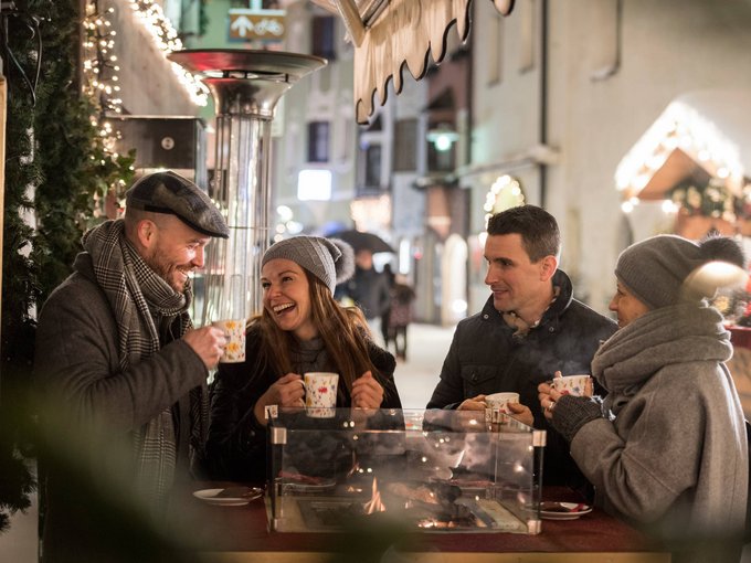 Your holiday in Vipiteno/Sterzing Four friends drinking hot drinks around a heated standing table in winter