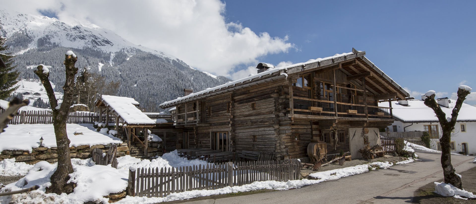 Urlaub anfragen Altes Holzhaus im Schnee mit Bergpanorama unter blauem Himmel