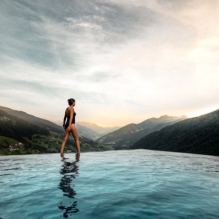 Wellness im Erlebnishotel Gassenhof Frau im Badeanzug am Rand eines Infinity-Pools mit Berglandschaft