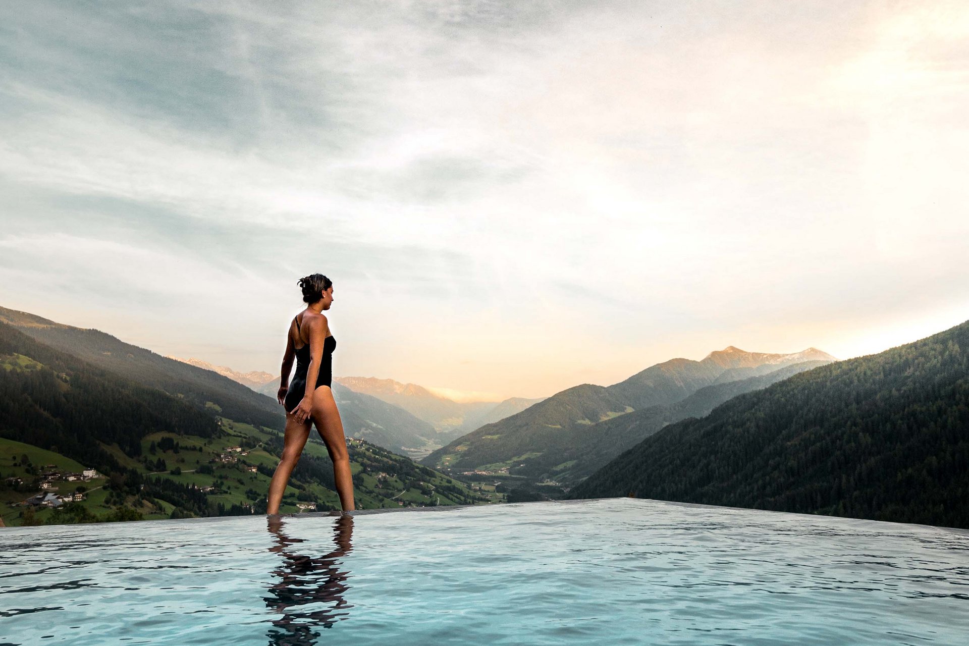 Urlaub anfragen Frau im Badeanzug am Rand eines Infinity-Pools mit Berglandschaft