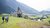 Familie wandert auf grüner Wiese bei kleiner Kapelle und Bergen im Hintergrund