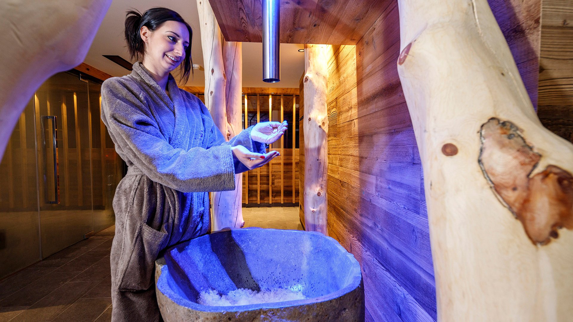 Our sauna realm Woman in bathrobe taking ice from a stone basin in a spa
