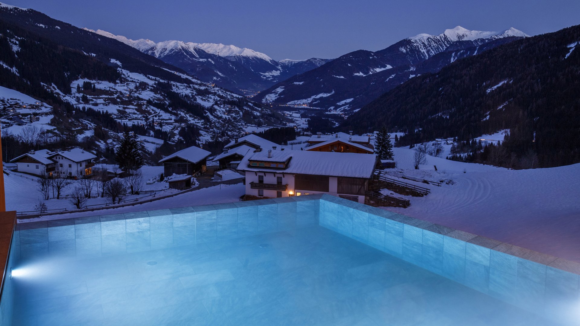 L’area wellness riservata agli adulti Piscina riscaldata con vista su un villaggio alpino innevato al crepuscolo