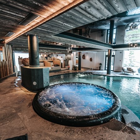 Wellness im Erlebnishotel Gassenhof Innenpool mit Whirlpool und moderner Holzdecke in einem Wellnessbereich