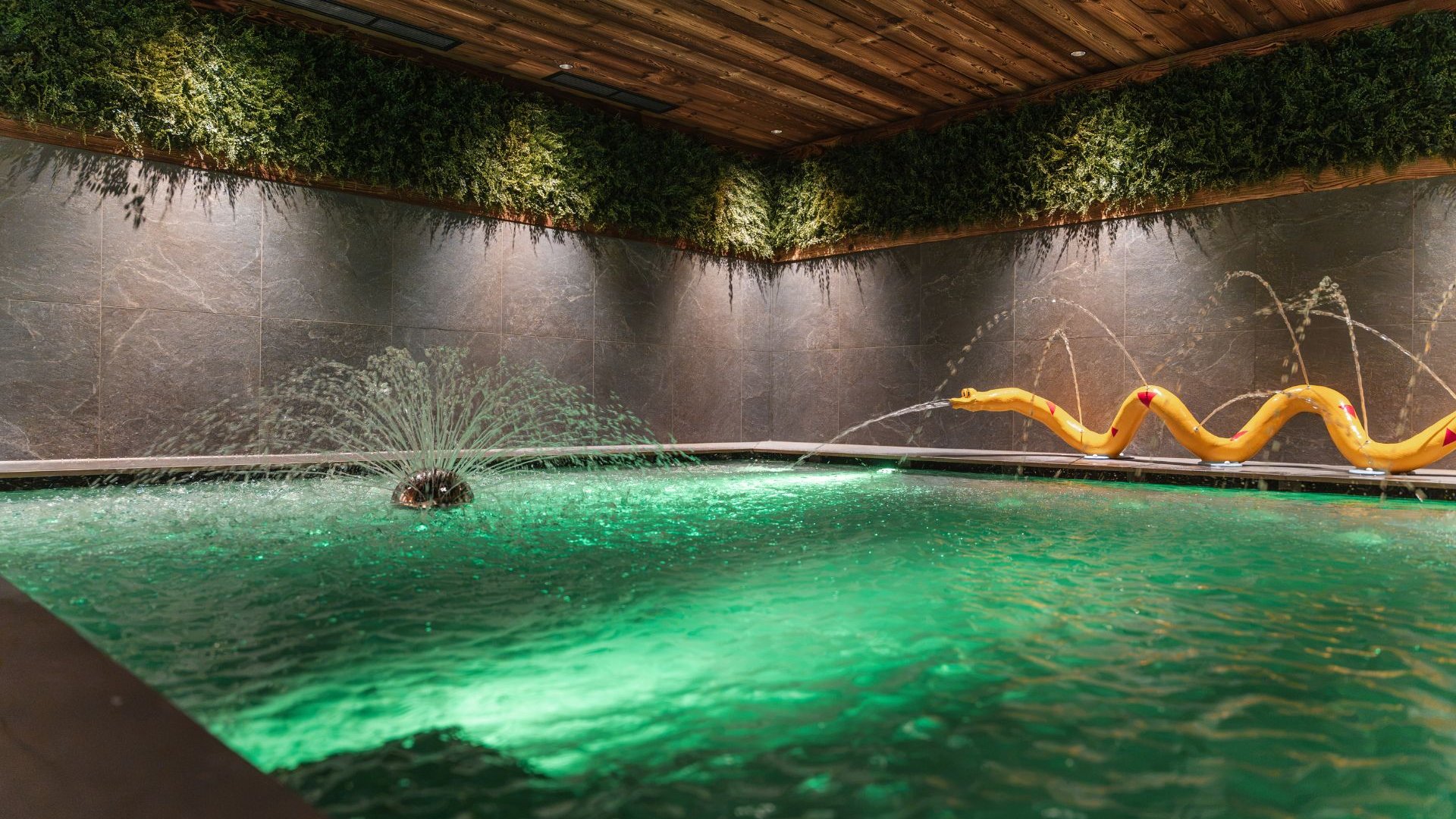 Familienurlaub im Gassenhof Beleuchtetes grünes Wasserbecken mit Springbrunnen und gelber Schlangenfigur