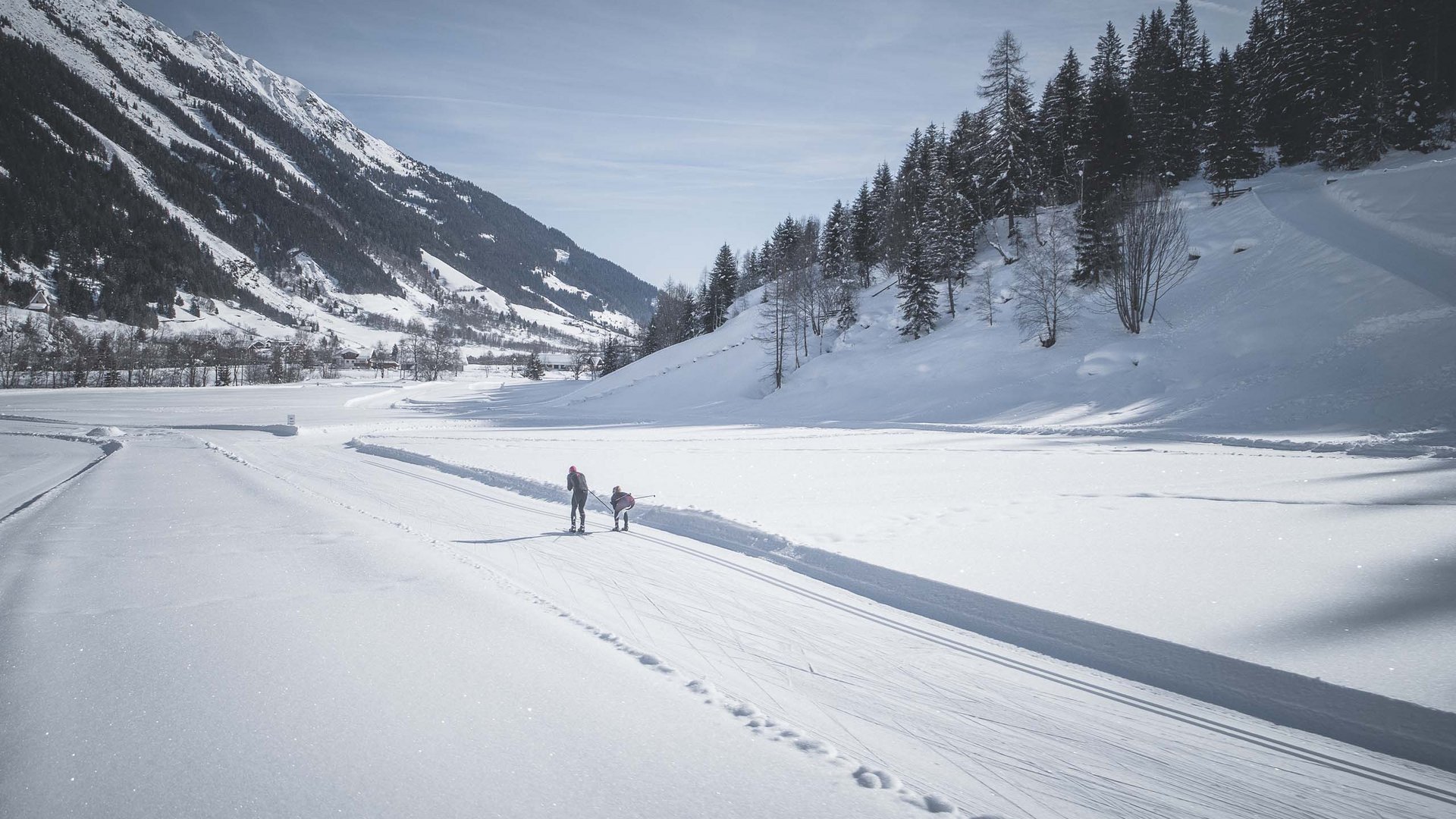 Zwei Skifahrer auf Loipe in verschneitem Bergtal bei Sonnenschein