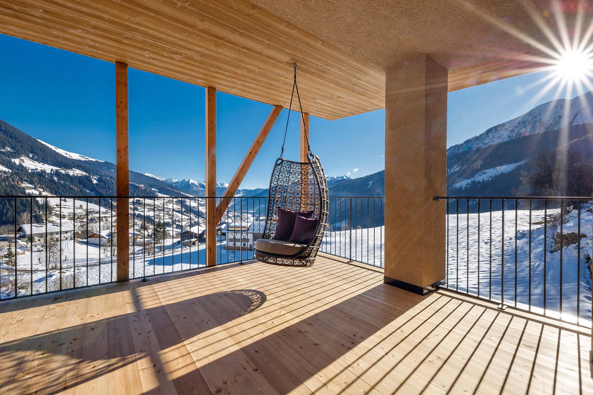 Urlaub anfragen Hängesessel auf Balkon mit Blick auf schneebedeckte Berge und sonnigen Himmel