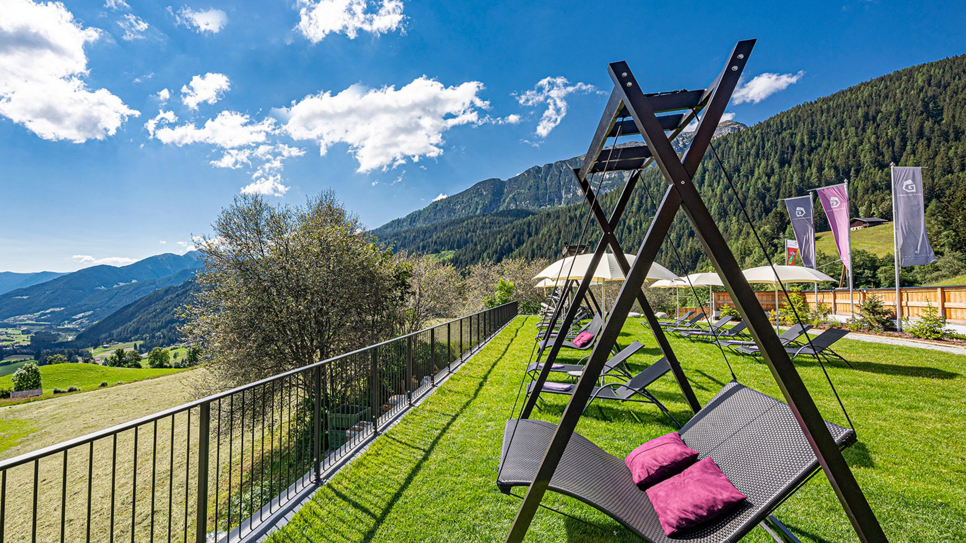 The best spot in the Ridnauntal valley Swing loungers on grass overlooking green mountains and valley under blue sky