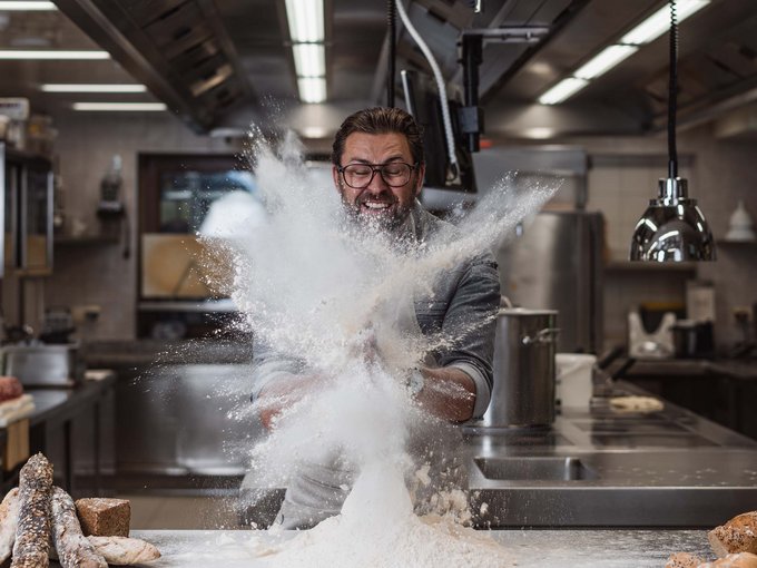 Arbeiten im Erlebnisort Gassenhof Bäcker wirbelt Mehl in einer professionellen Küche auf