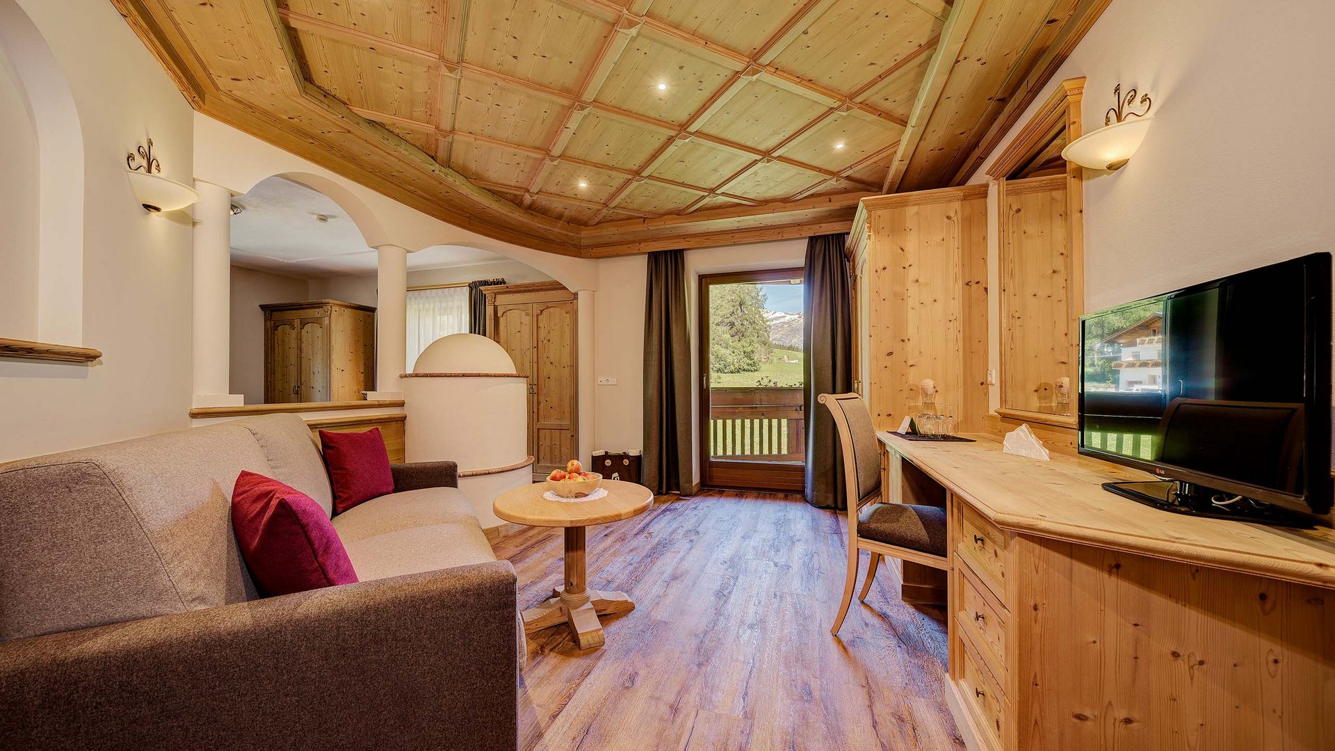 Zimmer und Suiten Gemütliches Wohnzimmer mit Holzmöbeln, Sofa, TV und Balkon mit Bergblick