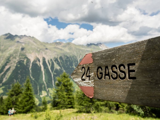 Our weekly programme Wooden sign with number 24 Gasse against mountain landscape and cloudy sky