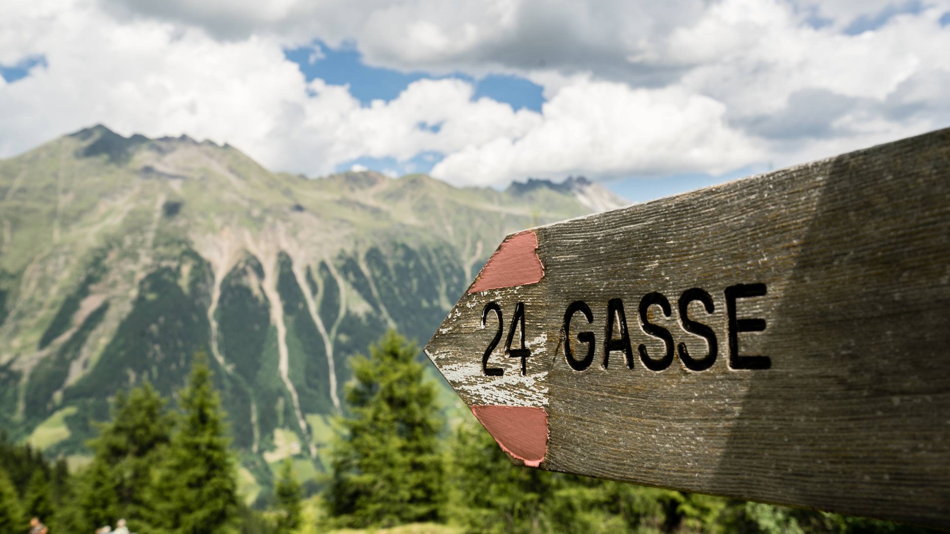 Summer hiking Wooden sign with number 24 Gasse against mountain landscape and cloudy sky