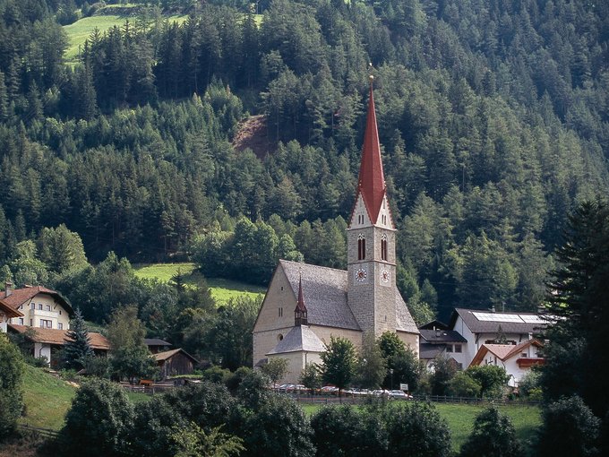 Urlaub im Wipptal Kirche mit rotem Turmspitz amid Wald und Häusern in einem Tal