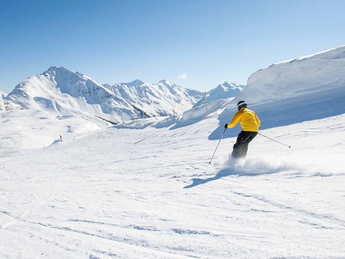 Your base for memorable experiences Skier in yellow jacket skiing down snowy mountain slope