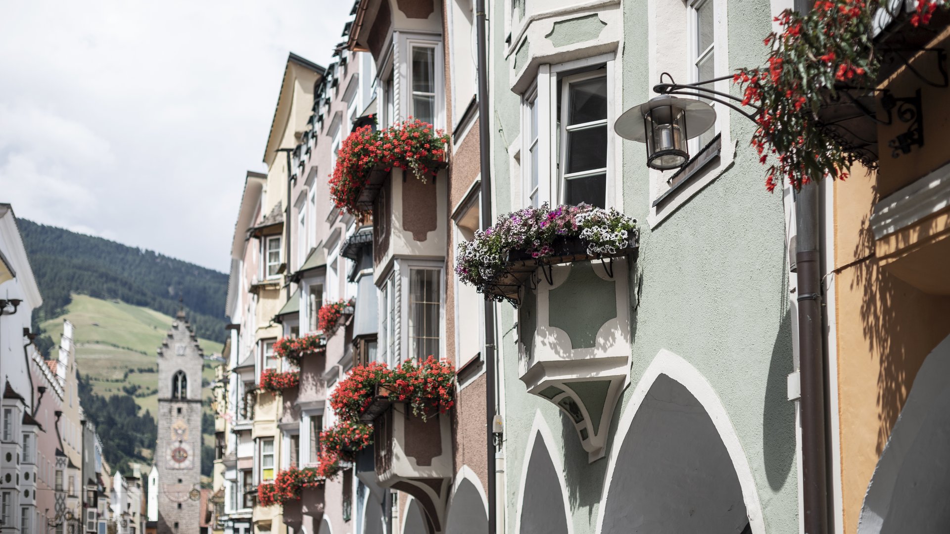 Urlaub bei Sterzing Bunte Häuser mit Blumenkästen und Bögen in einer Altstadtstraße mit Bergblick