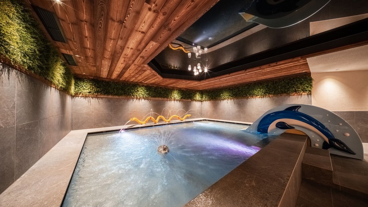 Gassenbadl: l’area wellness per famiglie Piscina coperta con fontana d’acqua, scultura di delfino e parete verde