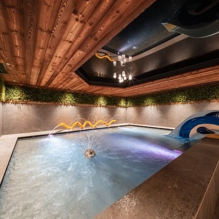 Wellness im Erlebnishotel Gassenhof Innenpool mit Wasserfontäne, Delfinfigur, Holzdecke und Pflanzenwand