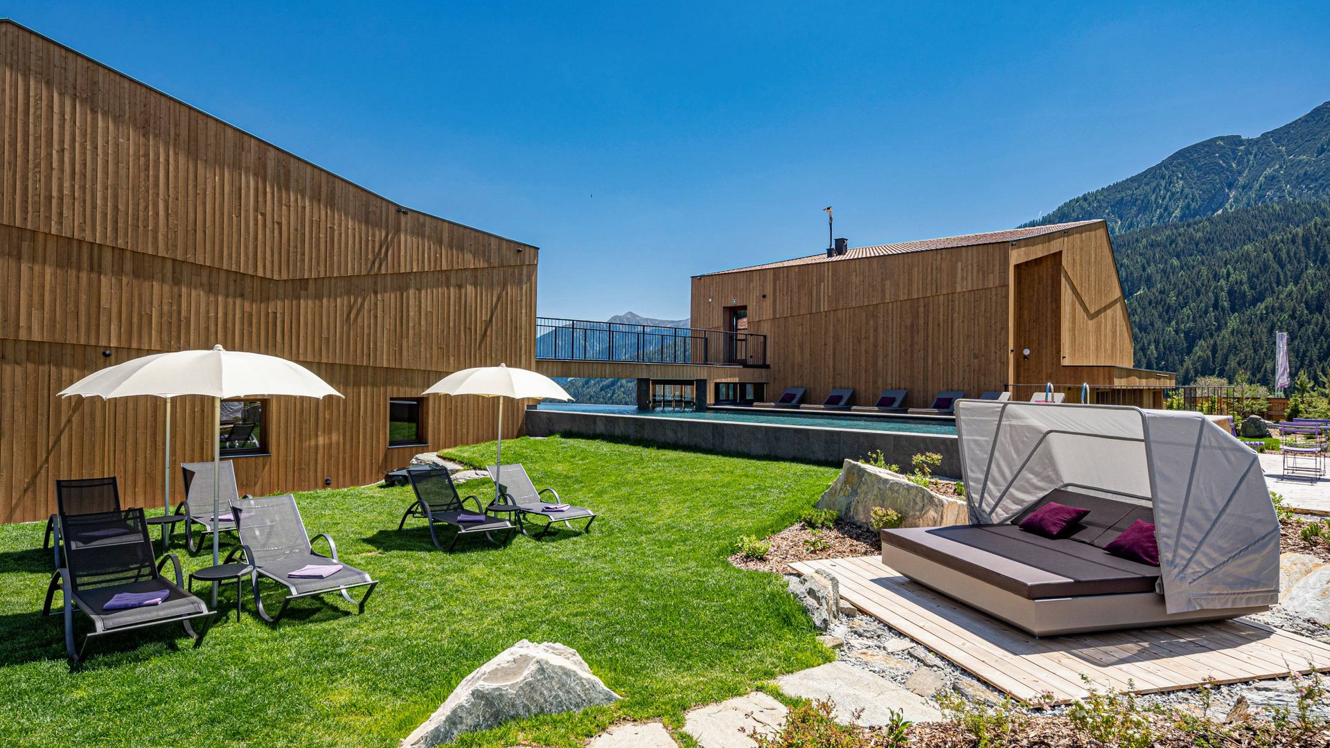 Hotel a Racines con centro benessere Case moderne in legno con lettini e ombrelloni su prato verde