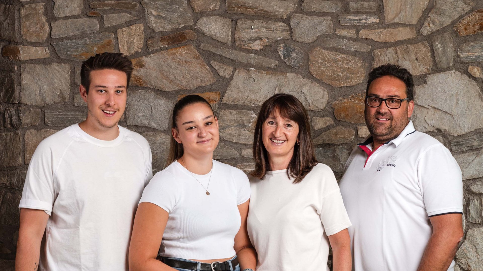 The Volgger family Four smiling people standing in front of a stone wall, casual clothing