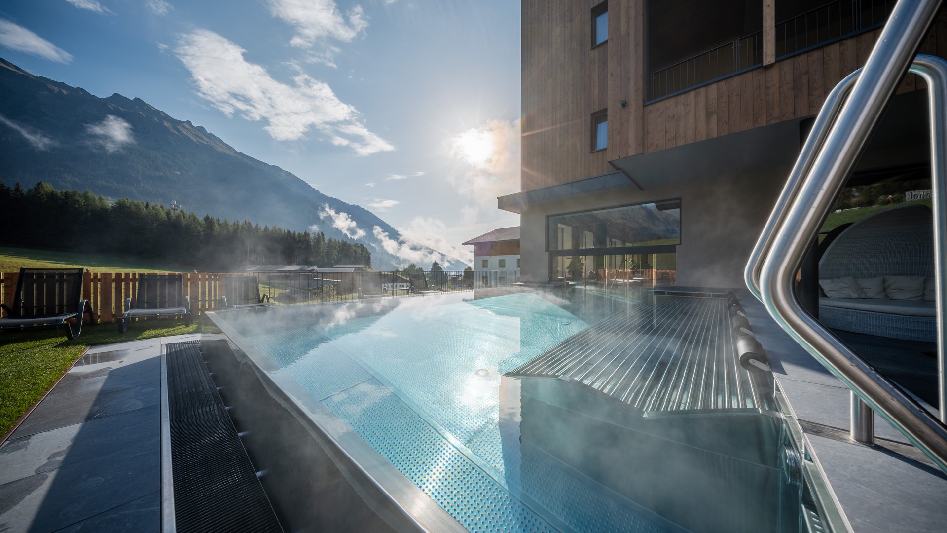 Hotel a Racines con centro benessere Piscina esterna riscaldata con vista sulle montagne accanto a un hotel moderno