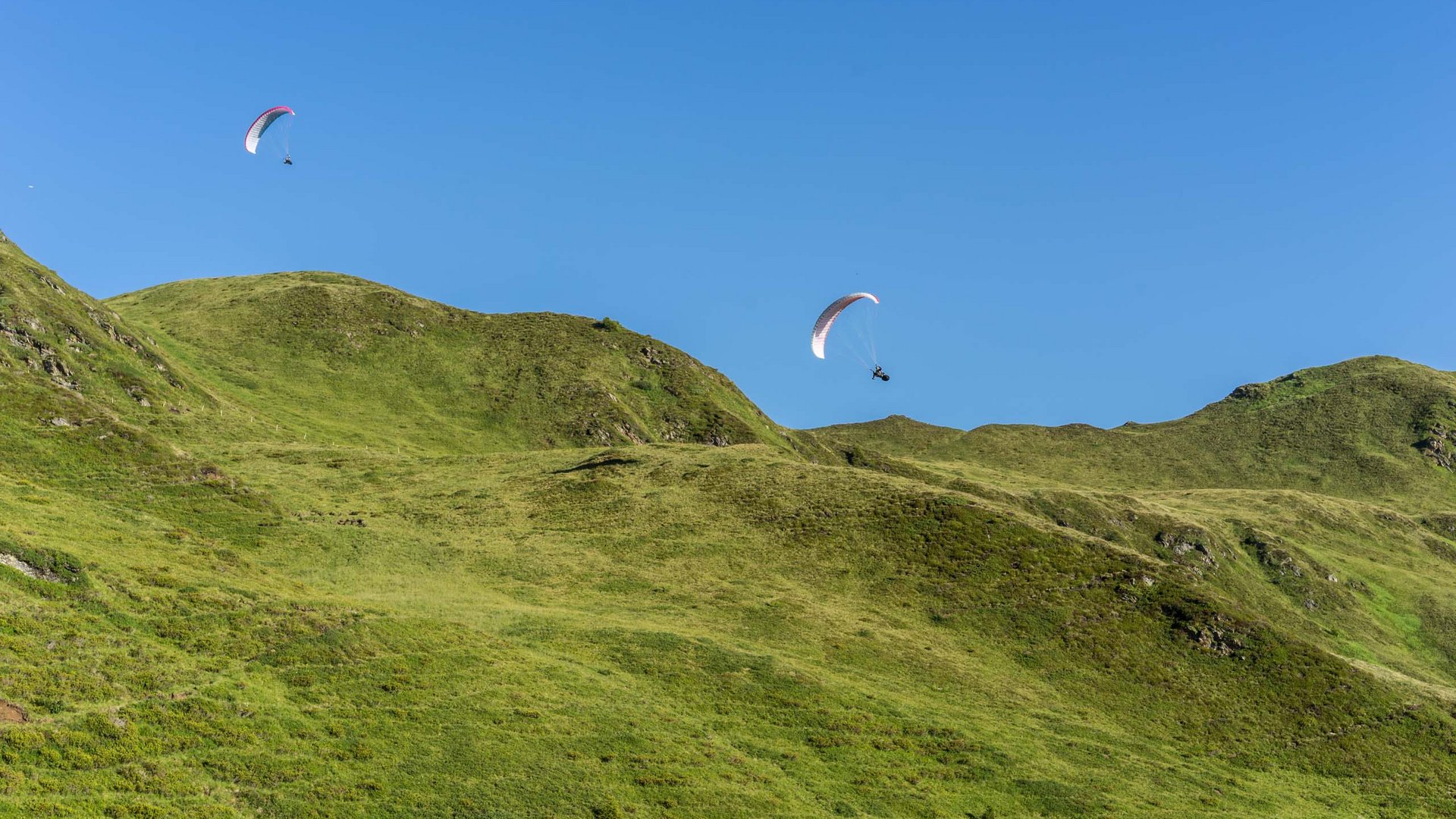 Due parapendii volano sopra colline verdi sotto un cielo azzurro