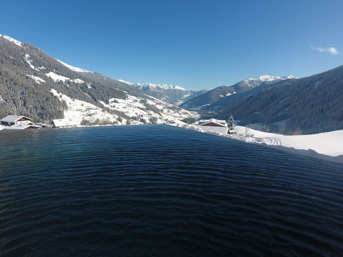 Hotel a Racines con centro benessere Piscina a sfioro con vista su montagne innevate e valle sotto cielo limpido