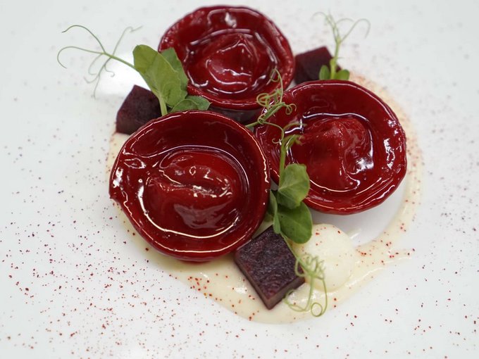 Der Erlebnisort Gassenhof Drei rote Ravioli mit Beilagen auf weißem Teller künstlerisch angerichtet