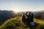 Zwei Personen sitzen auf einem Hügel und fotografieren den Sonnenaufgang über den Bergen