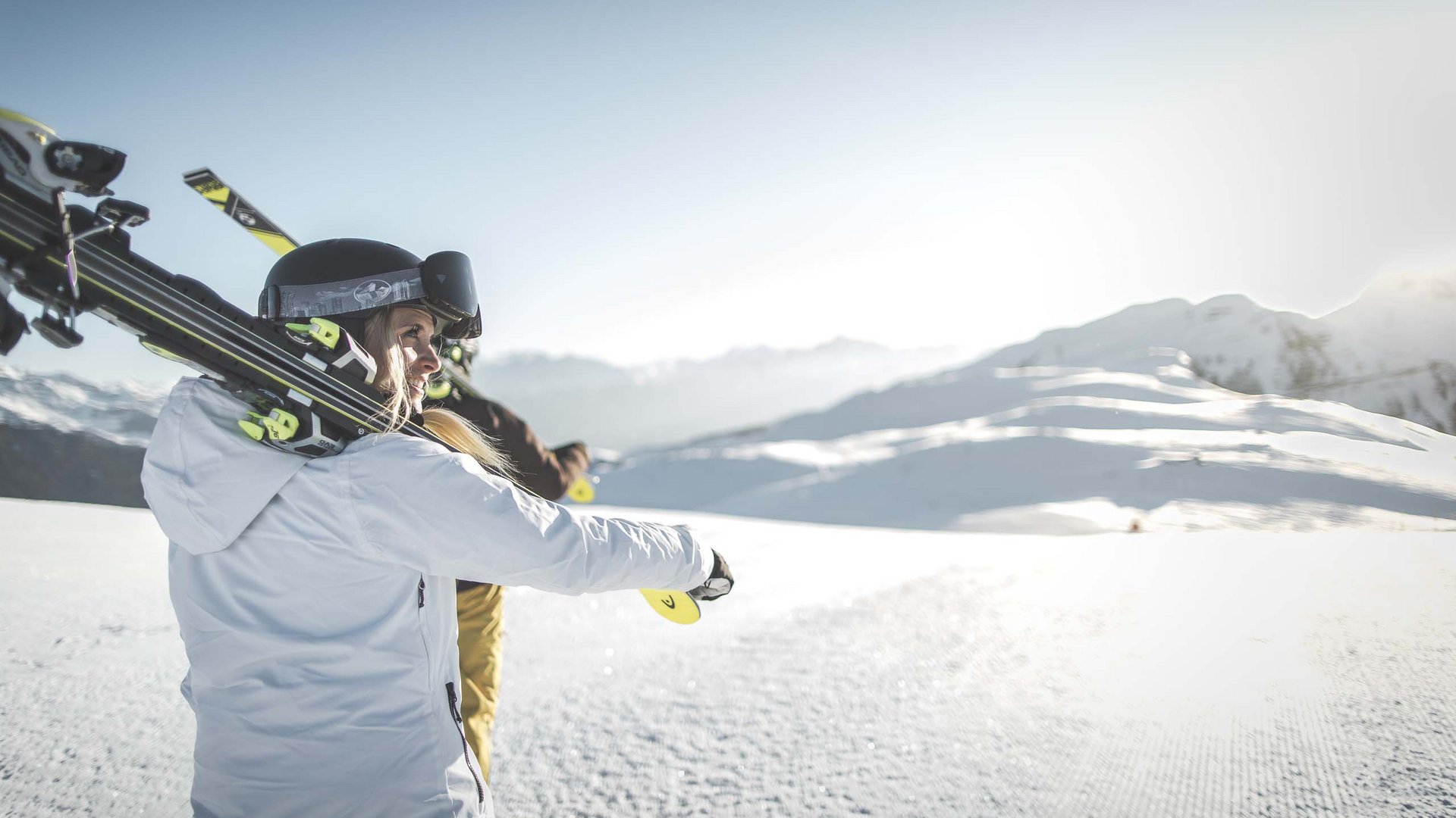Your ski holiday in South Tyrol Woman carrying skis over shoulder in sunny snowy mountain landscape