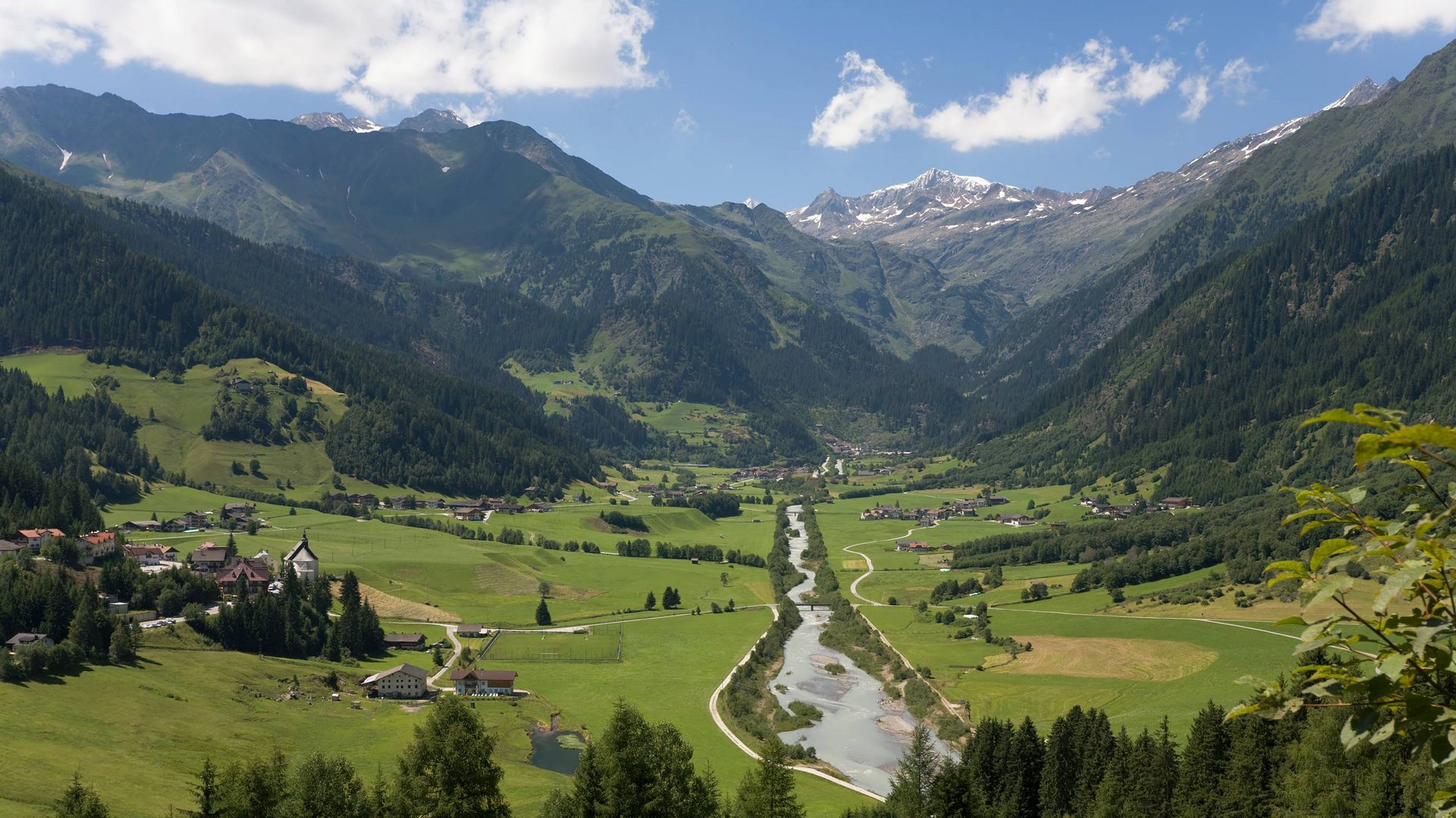 Your base for memorable experiences Valley with river and green meadows surrounded by mountains under blue sky