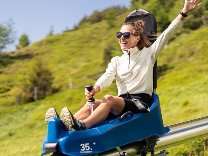 Sommerrodelbahn Rosskopf Frau mit Sonnenbrille fährt fröhlich auf einer Sommerrodelbahn im Grünen