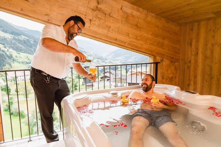 Cameriere | Cameriera Uomo nella vasca idromassaggio con petali di rosa e paperella, riceve birra su terrazza montana
