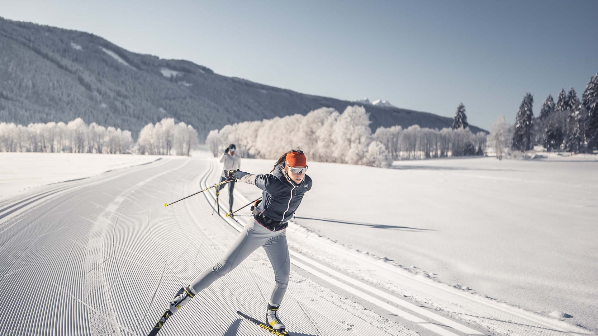 Your base for memorable experiences Two women cross-country skiing on groomed trail in snowy winter forest