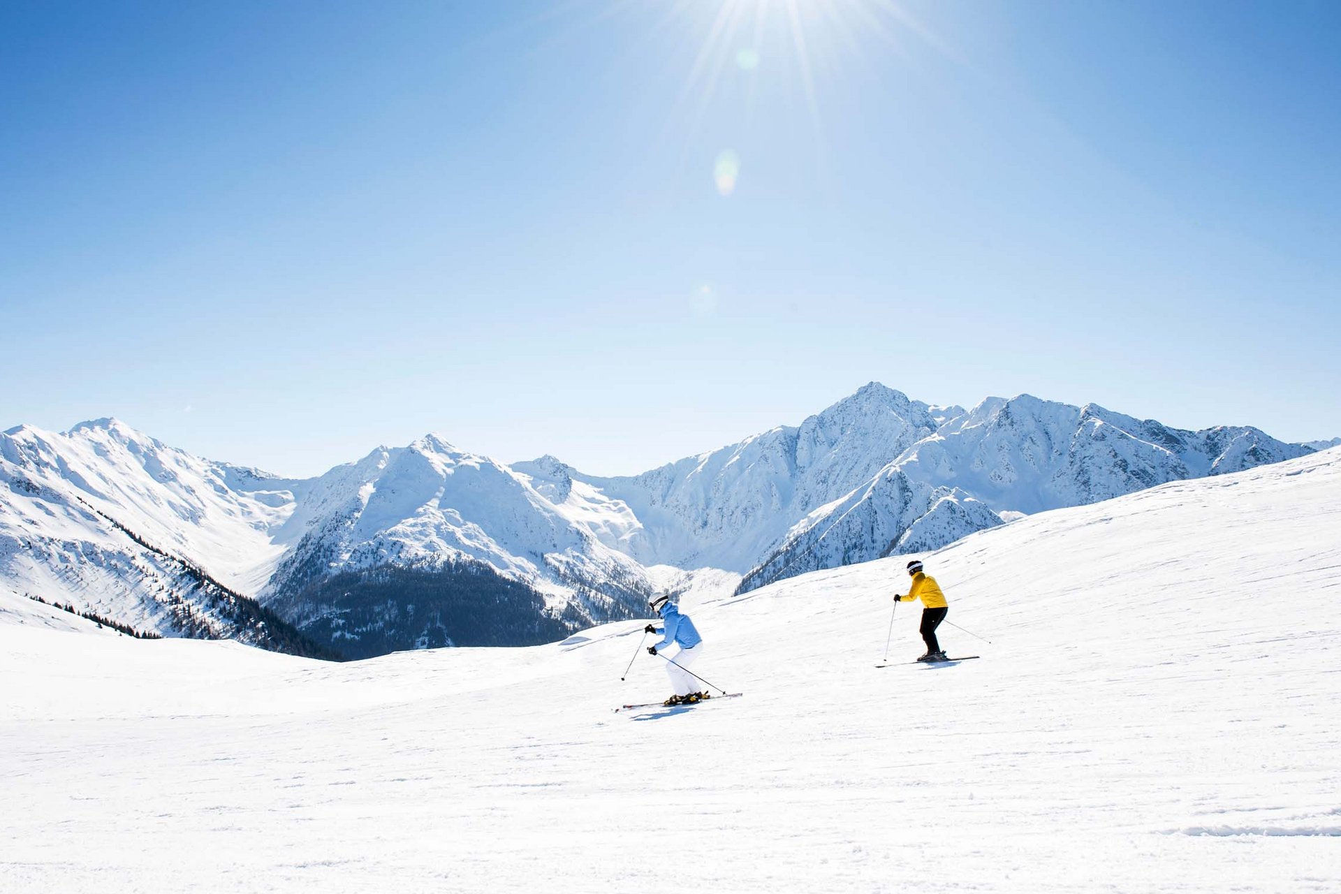 Urlaub anfragen Zwei Skifahrer auf verschneiter Piste mit Bergen bei klarem Himmel