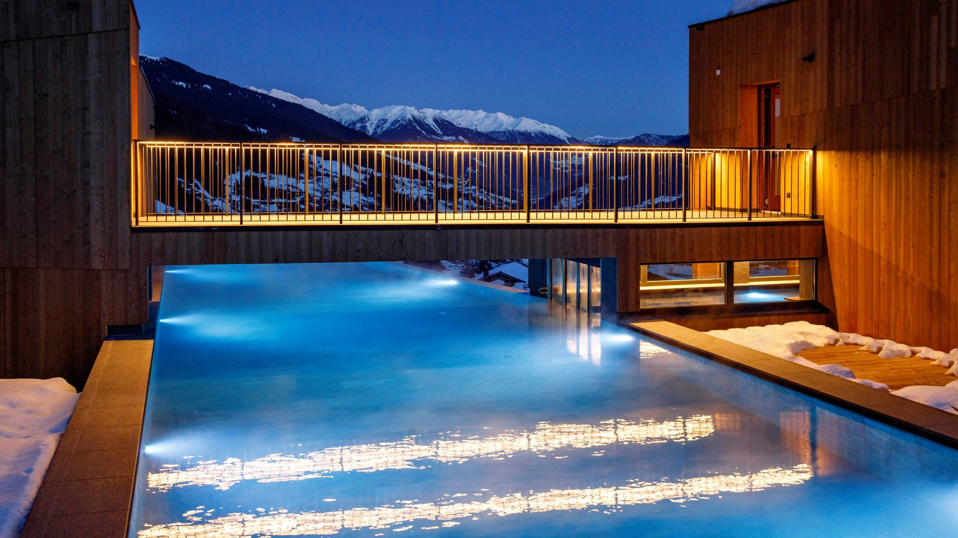 Hotel a Racines con centro benessere Piscina esterna illuminata di notte con vista sulle montagne e neve