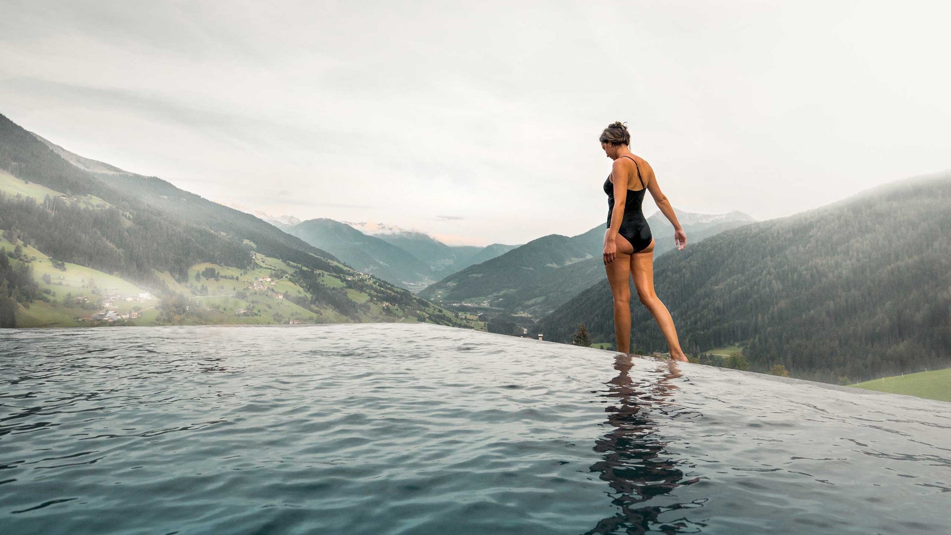 Hotel a Racines con centro benessere Donna in costume da bagno al bordo di una piscina a sfioro con vista sulle montagne