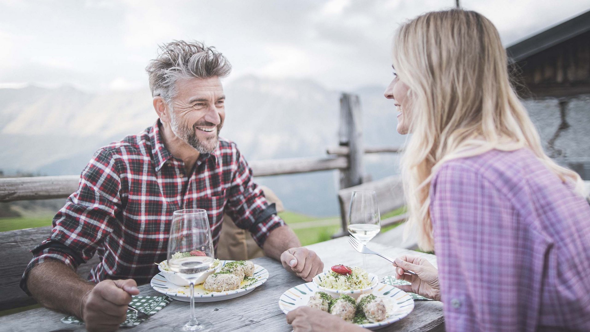 Mann und Frau essen draußen auf Holzbank mit Gebirgsblick.